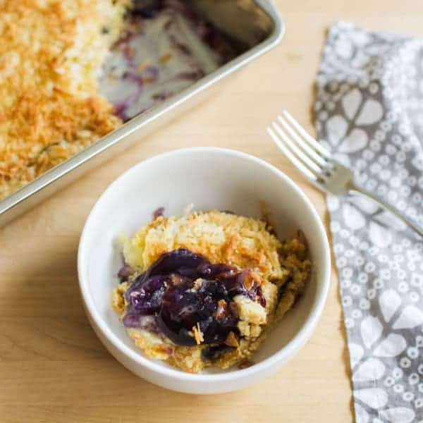 Small bowl of blueberry dump cake next to a pan next to a fork.