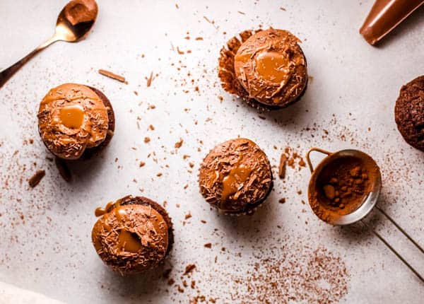 Overhead view of frosting cupcakes with a dab of caramel and cocoa powder on the counter.