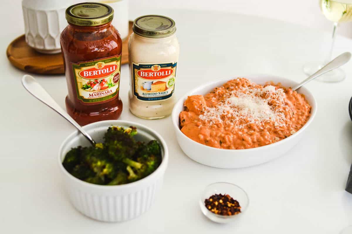 A bowl of farro topped with rosa sauce on a table next to jarred sauces and broccoli. 