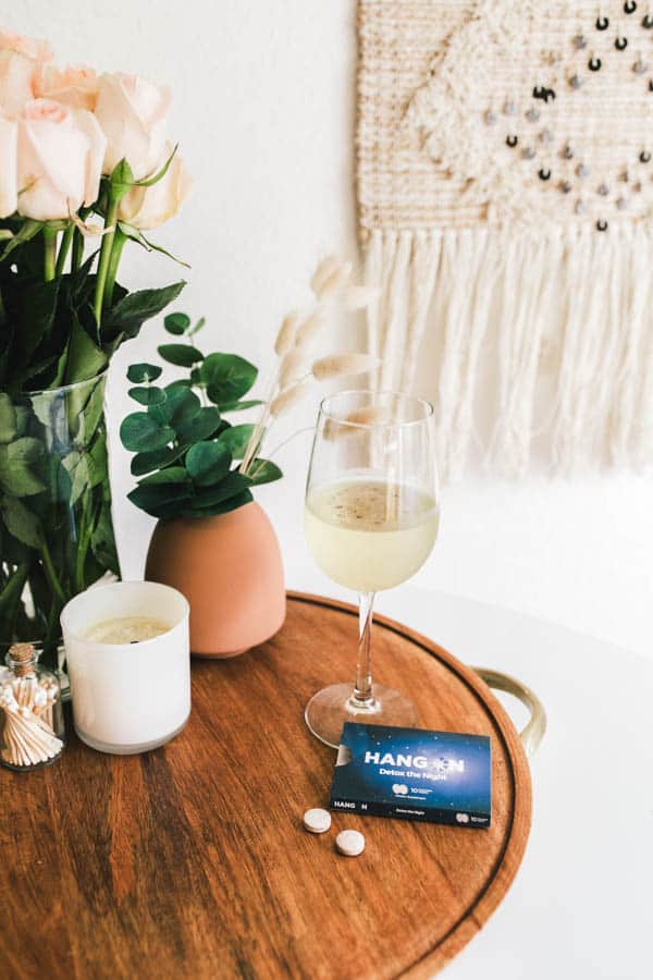 Close up of a glass of wine on a tray next to a hangover supplement.