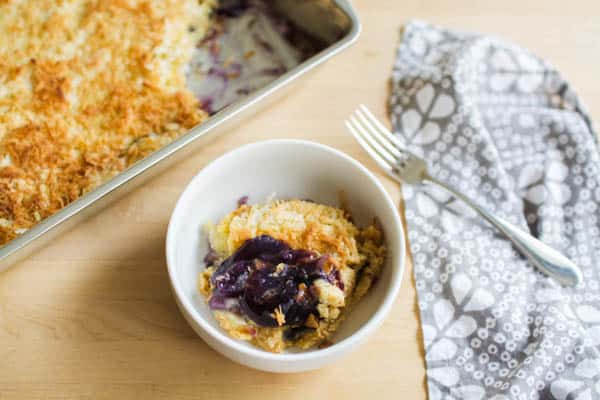 Dessert bowl with a serving of blueberry pineapple dump cake next to a pan of the finished dessert.