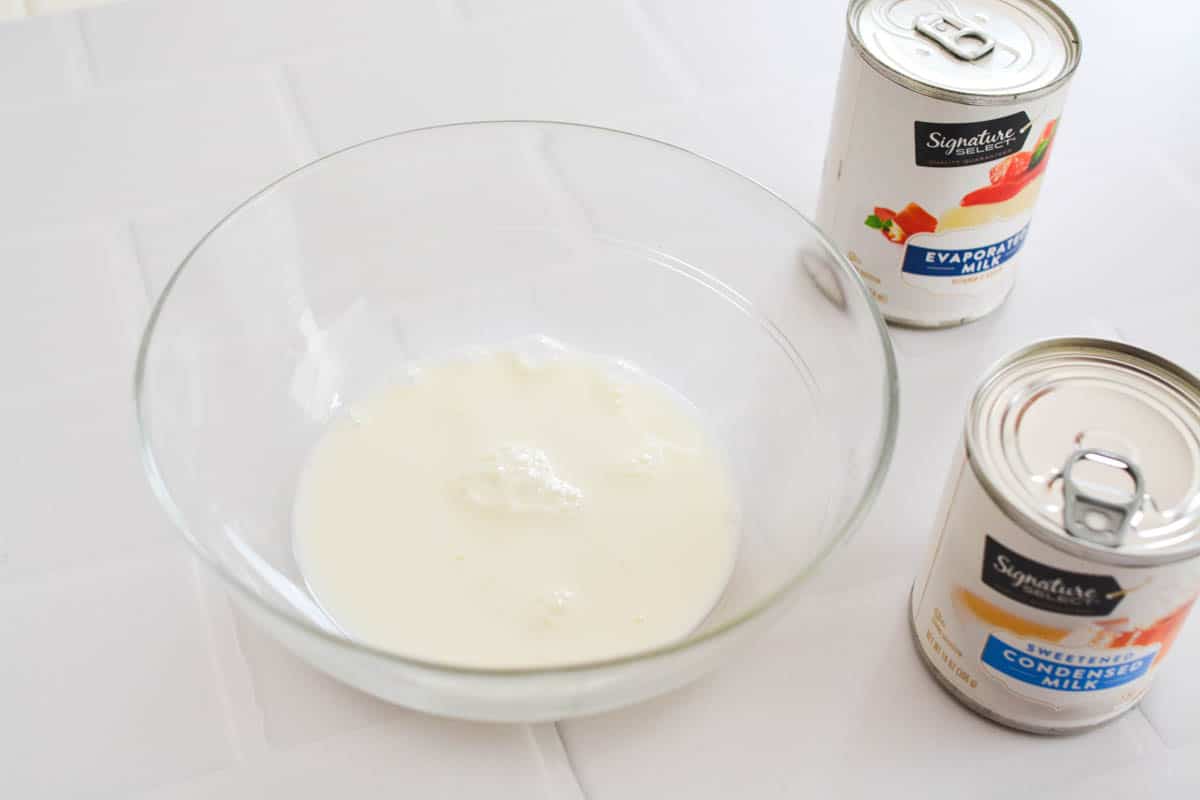 Close up of a glass bowl holding sweetened condensed milk next to a can of evaporated milk.