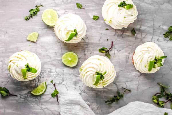 Overhead view of white frosted cupcakes garnished with mint and lime wedges.