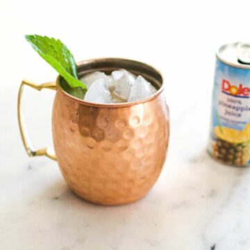 Mule mug garnished with mint with a can of pineapple juice in the background on a marble worktop.