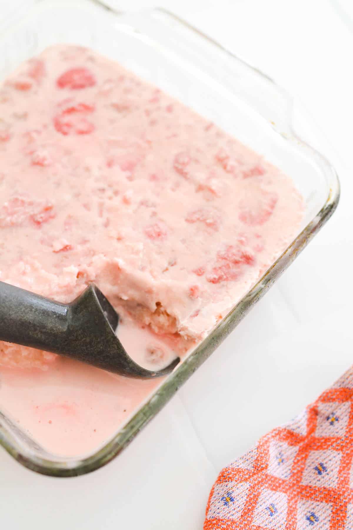 Close up of a frozen strawberry dessert with an ice cream scooper in it.