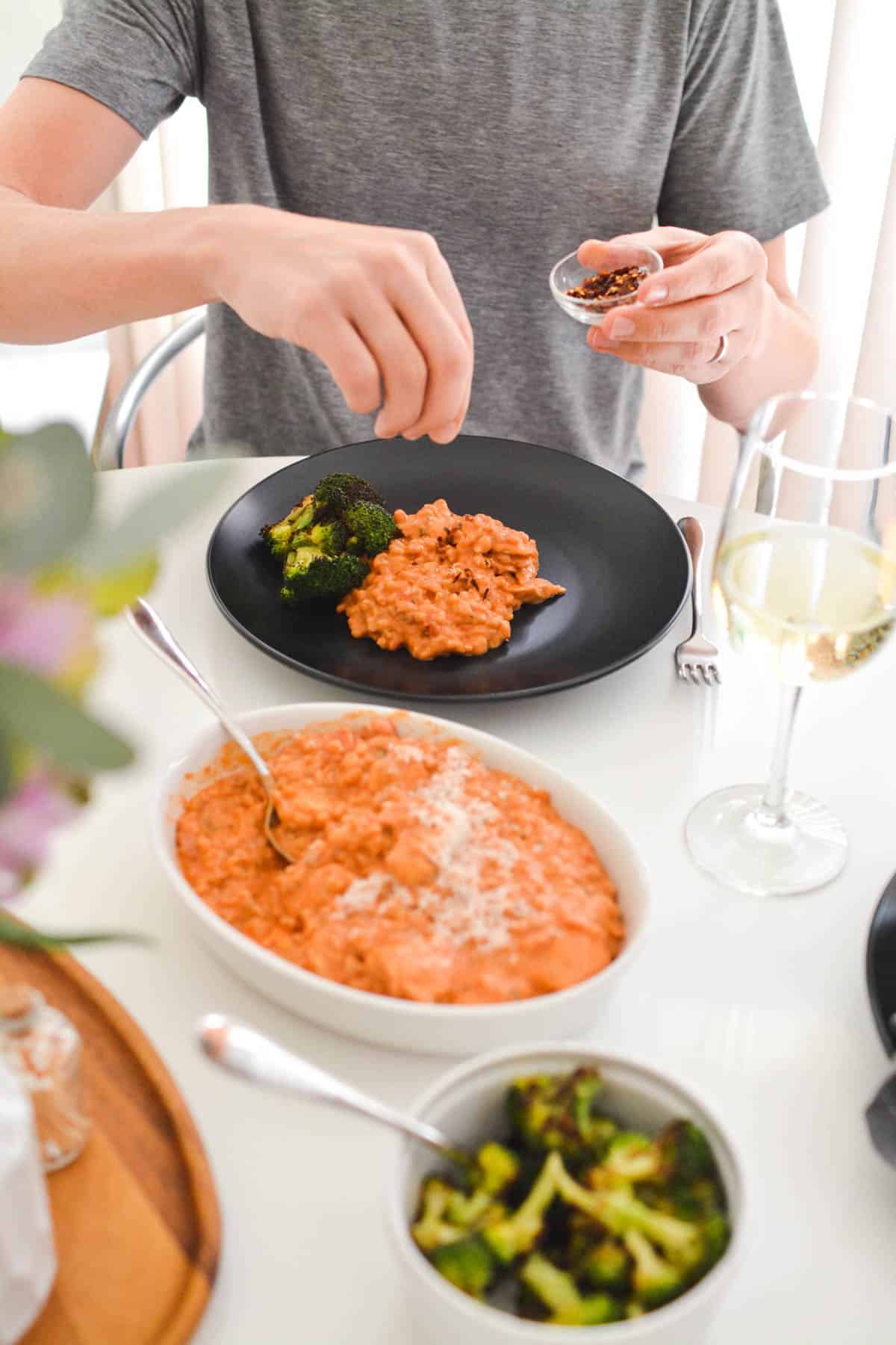 A man adding some red pepper flakes to his dinner.