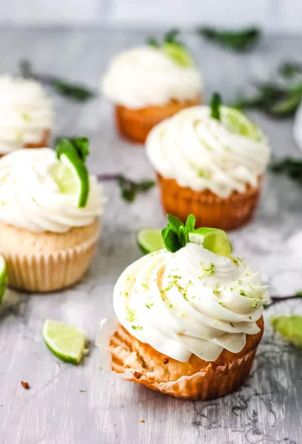 Frosted cupcakes on a table with lime and mint garnish.