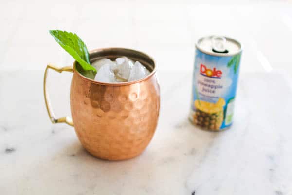 A Moscow Mule copper mug on a table next to a small can of pineapple juice.