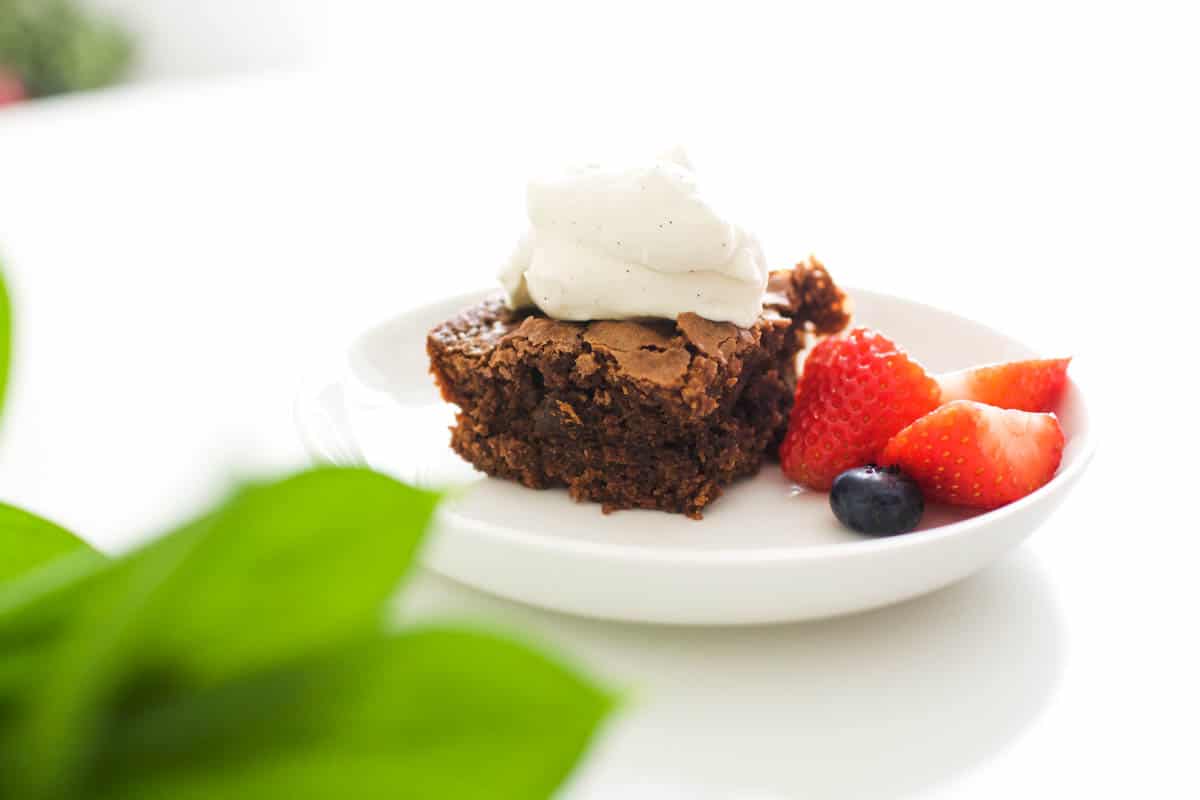 Close up of a small dessert plate with a brownie topped with whipped cream and berries.