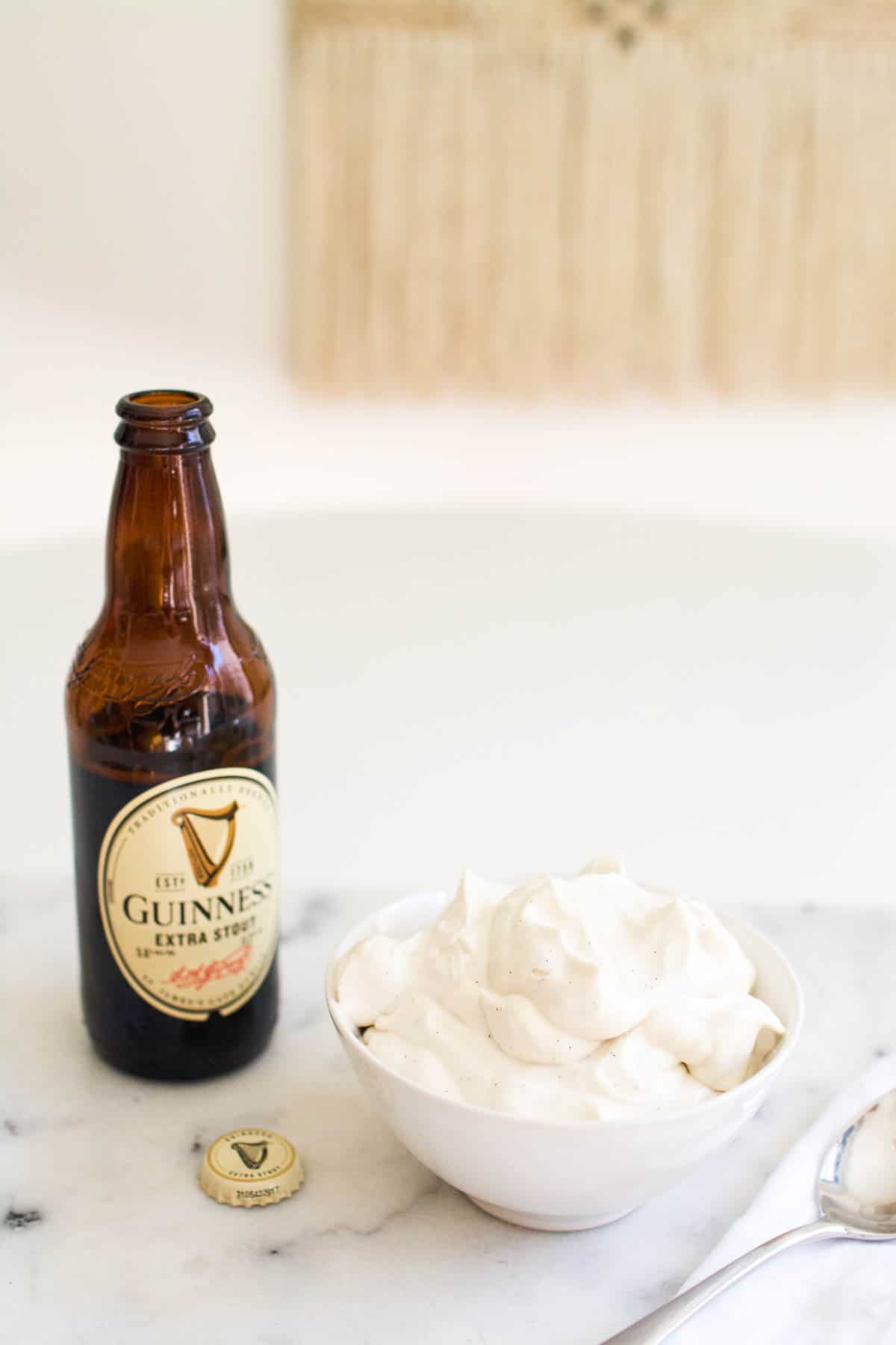 Close up of a bottle of Guinness on a counter next to a bowl of beer flavored whipped cream.
