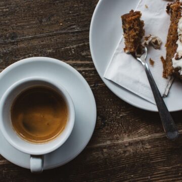 Overhead shot of a white coffee cup on a saucer next to a small plate with a baked treat.