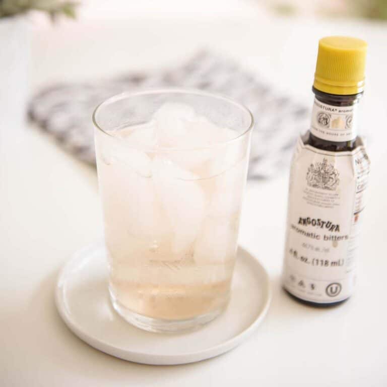 Close up of a short glass with Bitters and Soda on a table next to a bottle of cocktail bitters.