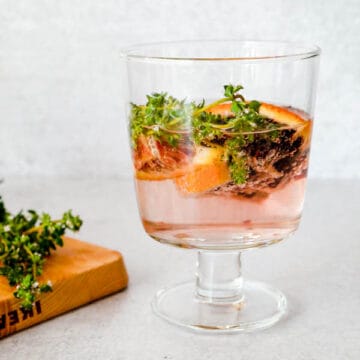 Blood orange and thyme white wine spritzer in a wine glass.