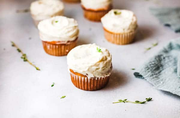 Lemon and Elderflower cupcakes on a table with a fresh herb garnish.
