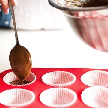 Close up of someone putting chocolate batter into a cupcake tin.