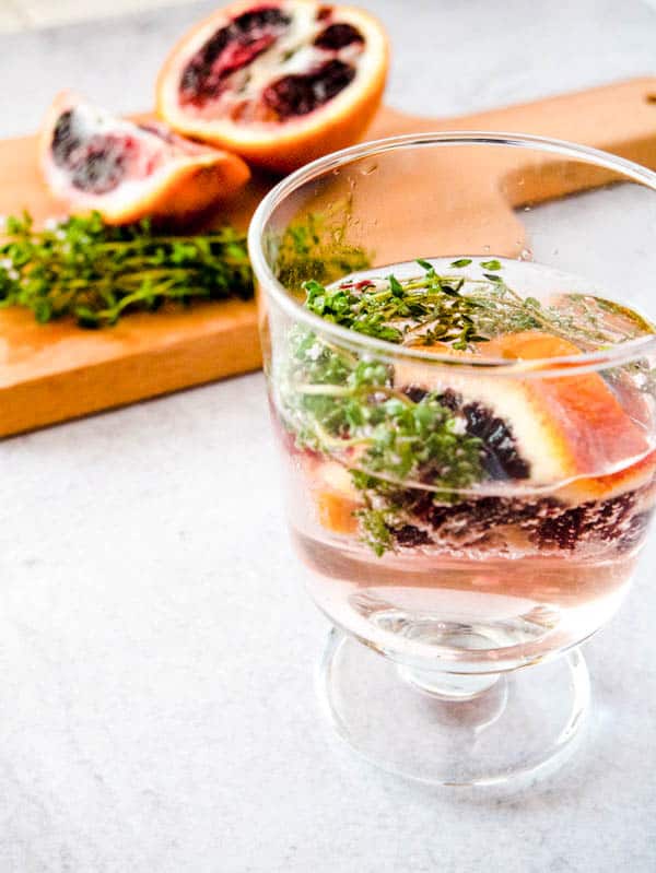 White wine spritzer in a glass with fresh thyme and pieces of blood orange.