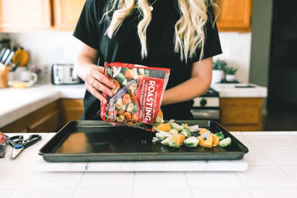 Woman adding frozen vegetables to a baking dish.