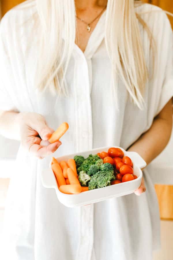 Woman holding a rectangle bowl with fresh veggies.