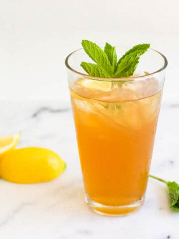 Tall glass of iced tea with mint garnish and lemon wedges next to it.