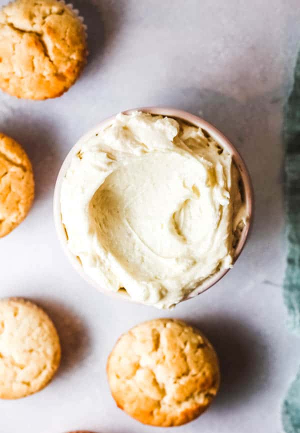 Bowl of lemon buttercream next to unfrosted cupcakes.