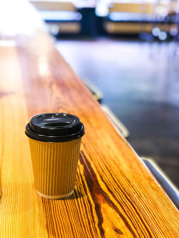 Cup of coffee in a to-go cup on a wooden counter.