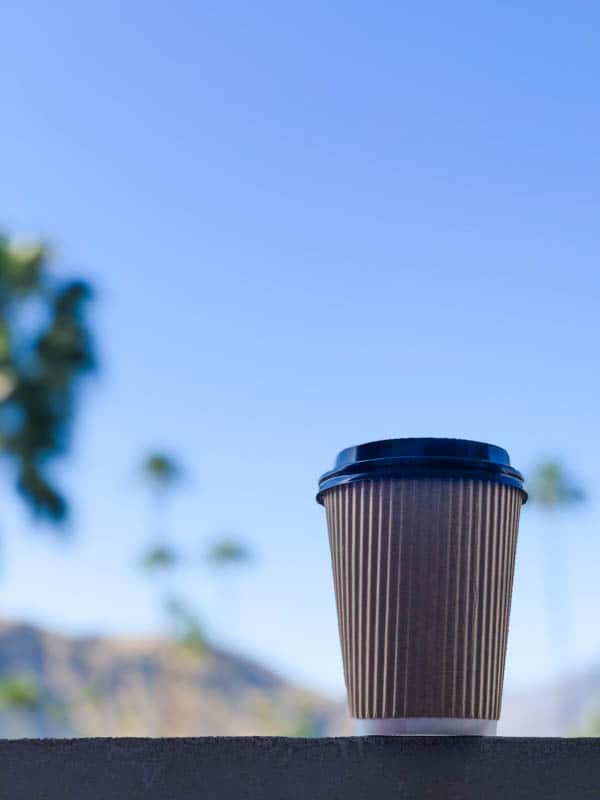 Close up of a coffee cup with sky and palm trees in the background. 