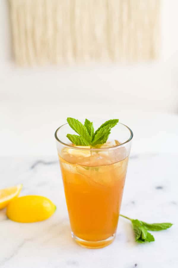 Close up of a glass of iced tea with a mint garnish and lemon wedges.