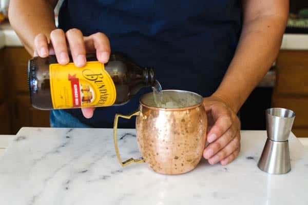 Woman pouring ginger beer into a copper mug with rum for a Moscow Mule.