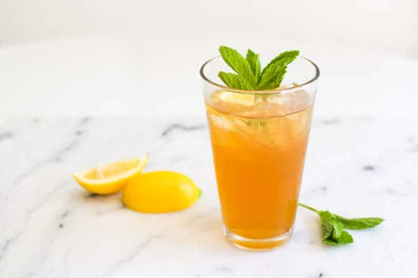 Tall glass with iced tea next to lemon wedges and a mint garnish. 