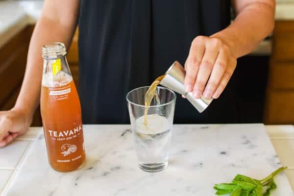 Woman adding iced tea to a tall glass with vodka. 