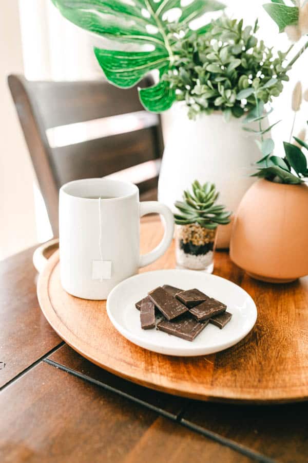 A tray with a cup of tea, a plate of chocolate and some small plants.