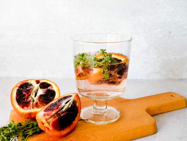 Stemmed glass with a blood orange wine spritzer on a cutting board next to a cut open blood orange.