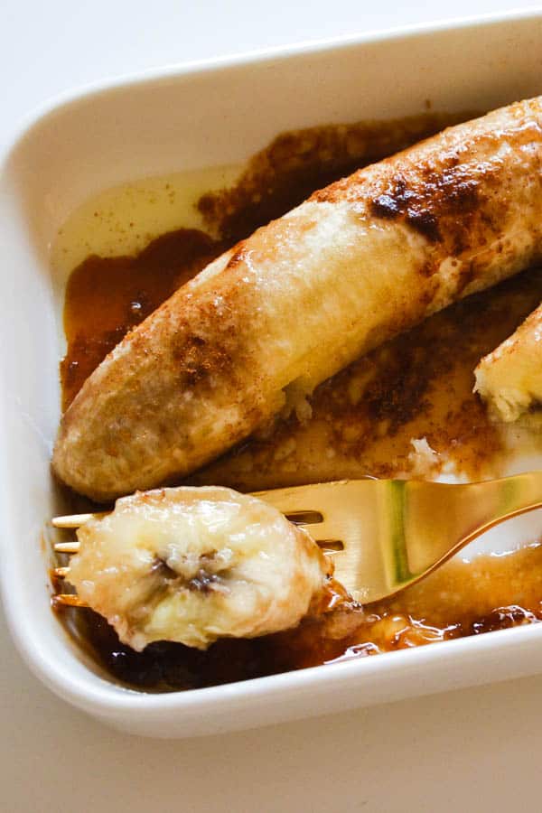 Baked bananas with brown sugar and cinnamon with a slice on a fork.