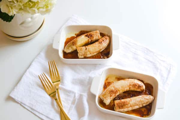 Bananas baked with butter and brown sugar in small baking dishes on a table next to forks.
