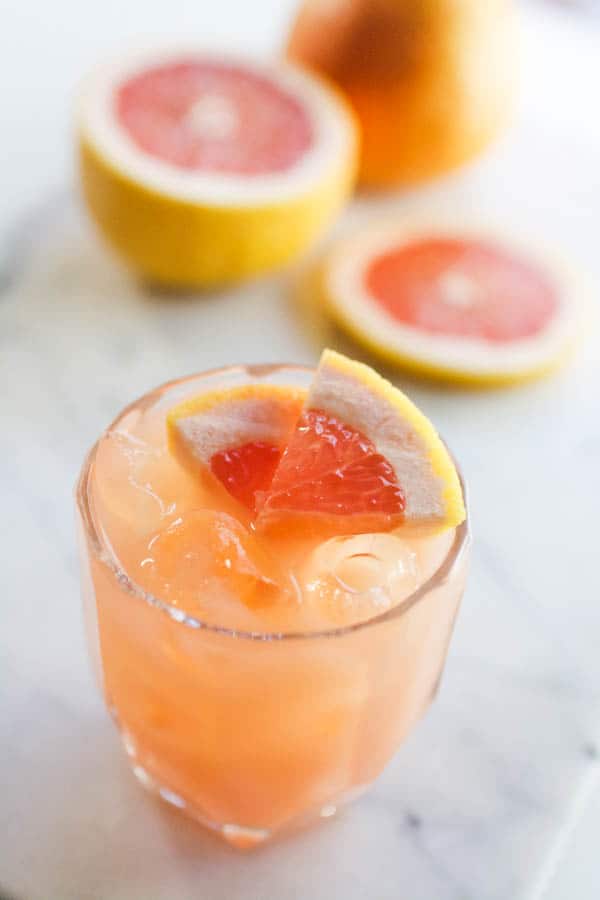 A cocktail on a table with grapefruit behind it.