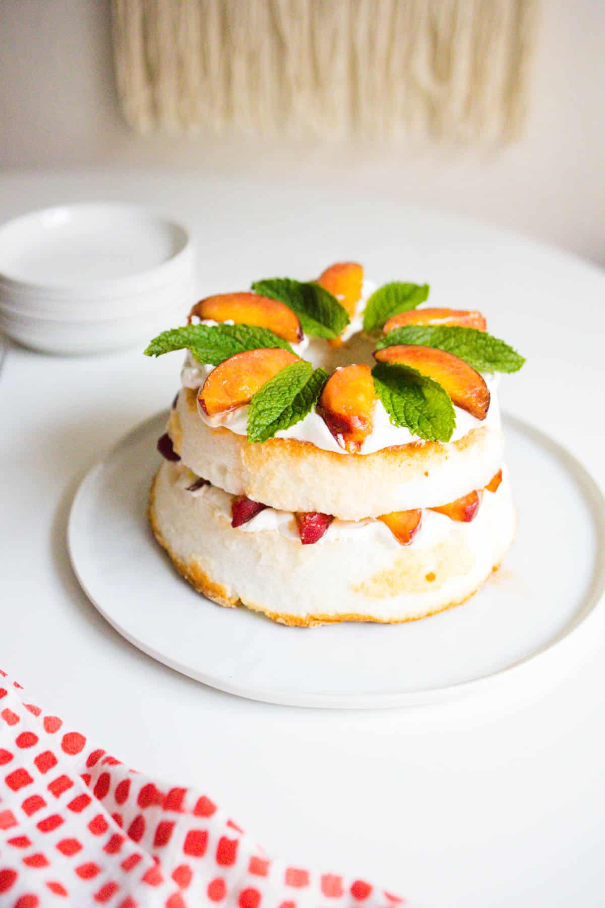 A semi homemade dessert with store bought angel food cake cut and layered with Cool Whip and peaches then topped with mint.