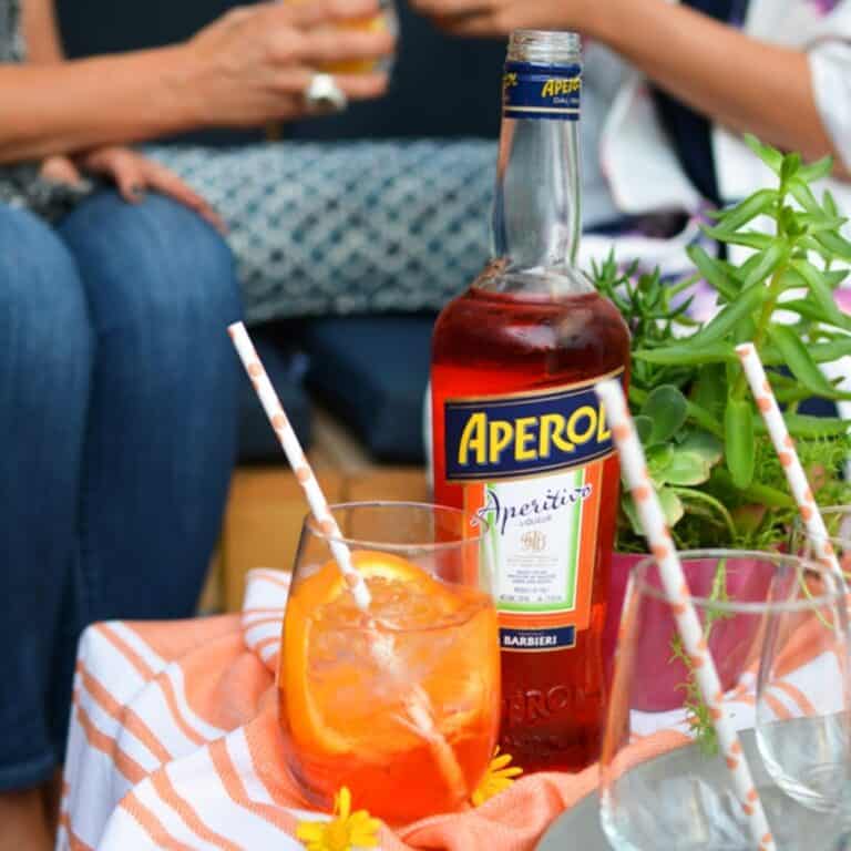 Close up of a glass with an Aperol Spritz cocktail next to a bottle of Aperol.