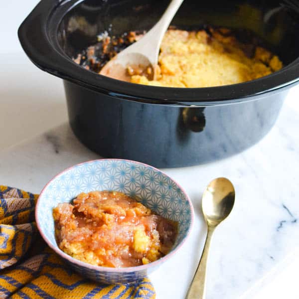 Apple dump cake in a crockpot with a serving next to it in a blue starburst bowl.