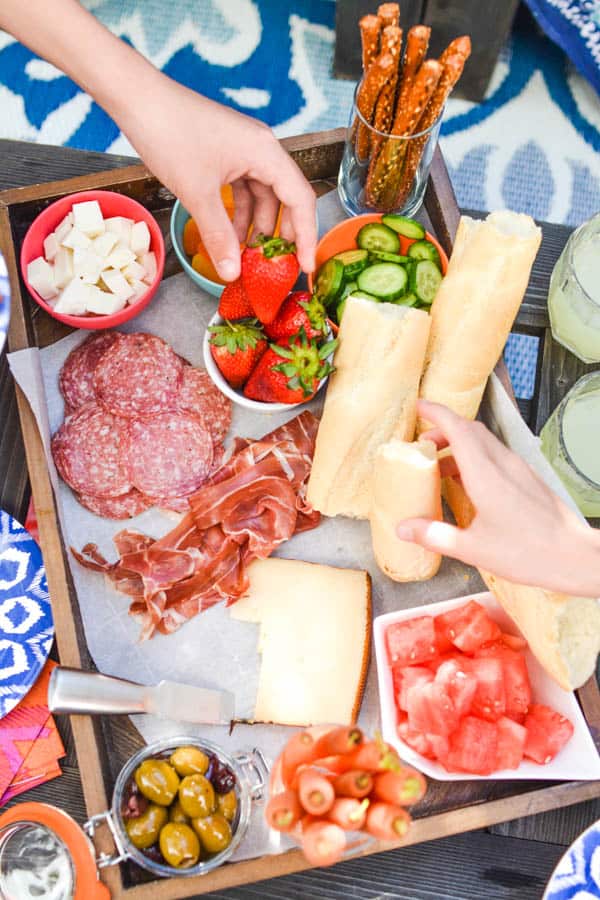 Kid's hands reaching for snacks on a snack board with meats and cheese.