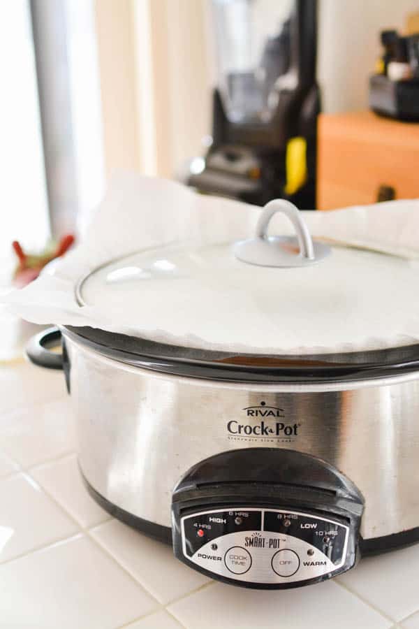 The outside of a slow cooker with a paper towel under the lid for cooking a dump cake