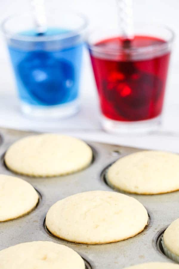 A pan of baked white cupcakes next to red and blue Jello
