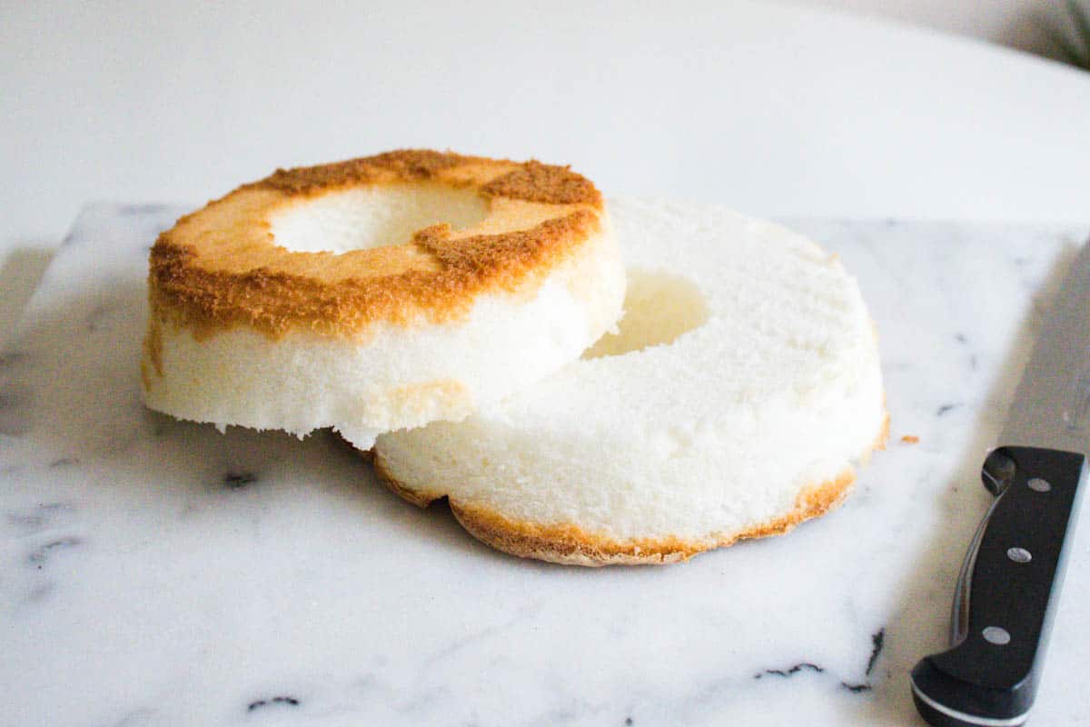 An angel food cake sliced in half on a cutting board next to a knife.