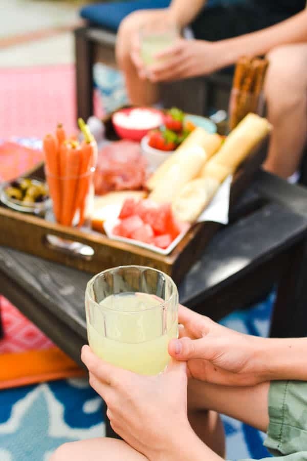 Child's hand holding a glass of lemonade with a snack tray in the background.