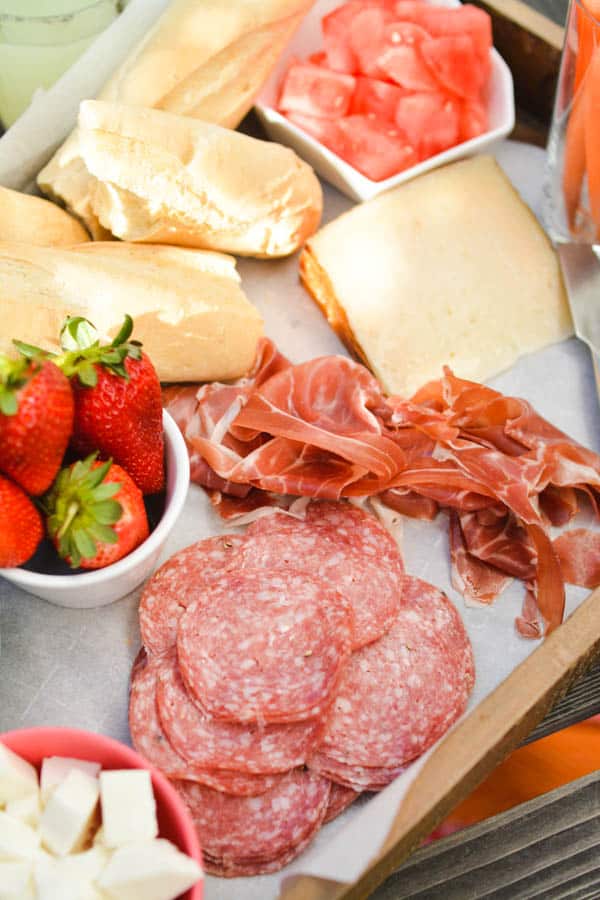 A tray of food on a table, with Salami, Prosciutto, and cheese.