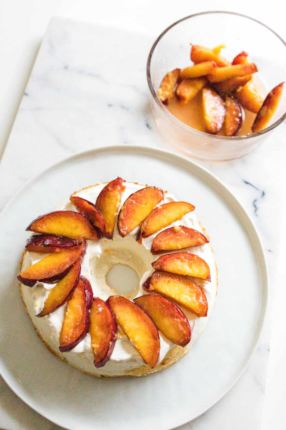 Sliced peaches laying in a pattern on top of a half of angel food cake.