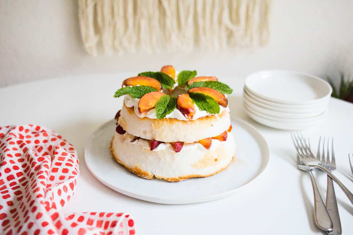 A layered angel food cake with peaches that have been sweetened with sugar and ginger and topped with fresh mint.