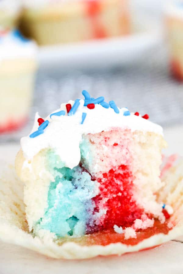 A red, white and blue cupcake cut in half on a table so you can see the colors of the cake inside.