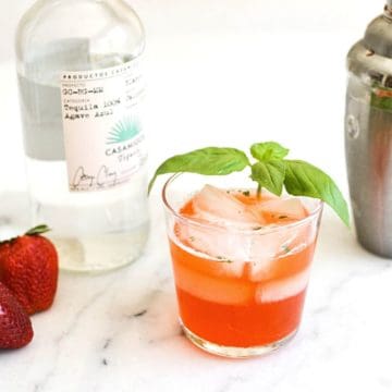 A short cocktail glass holding a Strawberry Basil Margarita on a table.