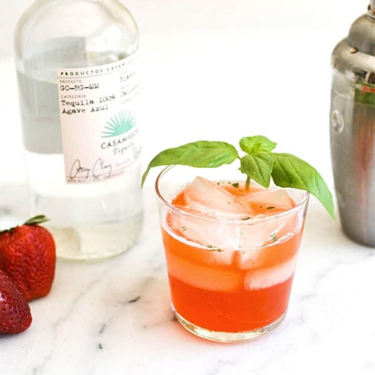 A short cocktail glass holding a Strawberry Basil Margarita on a table.