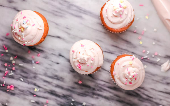 Frosted rosé cupcakes on a marble table with pink and white sprinkles. 